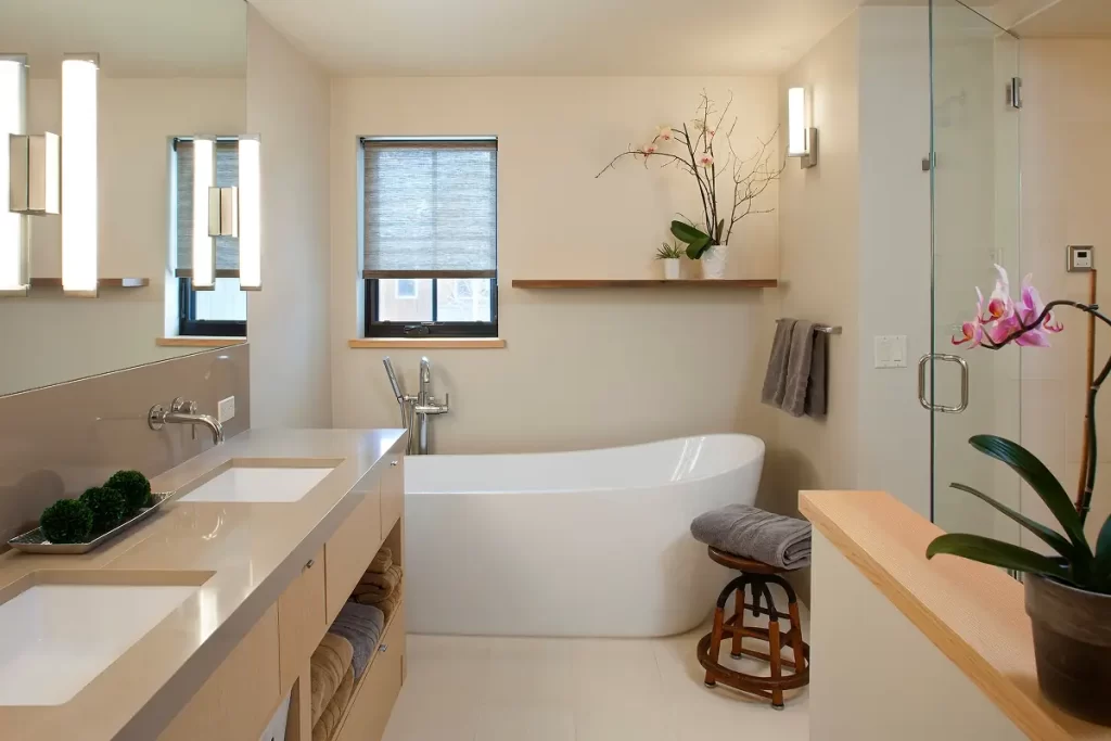 Minimal modern bathroom with freestanding tub, dual sinks, and natural light from two windows.