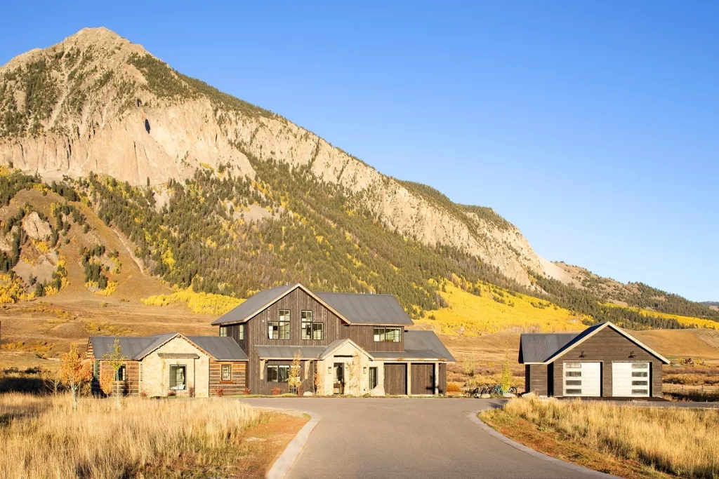 Modern mountain home in Crested Butte with dark siding and stone, surrounded by golden fall foliage.