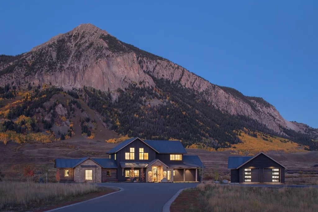 Nighttime view of a custom home in Aperture, Crested Butte with lit gables and a detached garage.