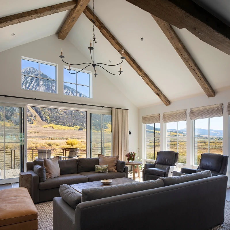 Mountain-view great room with vaulted ceilings, exposed timber beams, and panoramic glass doors to deck.