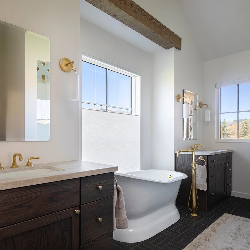 Modern bathroom with a freestanding tub, dark wood vanities, brass fixtures, and clerestory light.