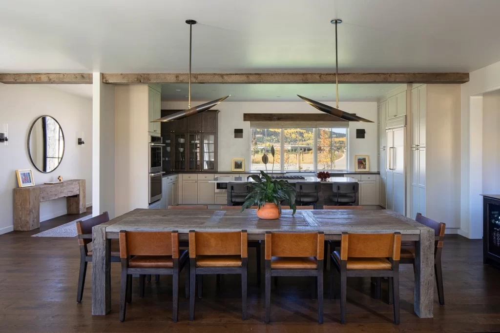 Rustic modern dining room with wood beams and leather chairs, open to a custom kitchen with large windows.
