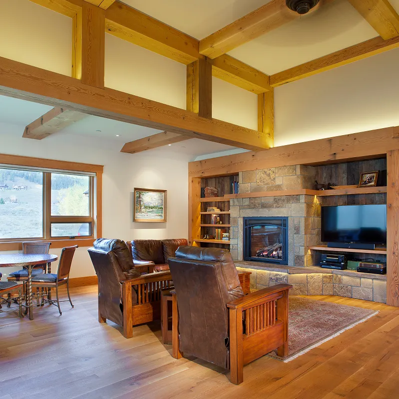 Warm family room with stone fireplace, built-in shelving, and leather furniture overlooking exterior mountain views.
